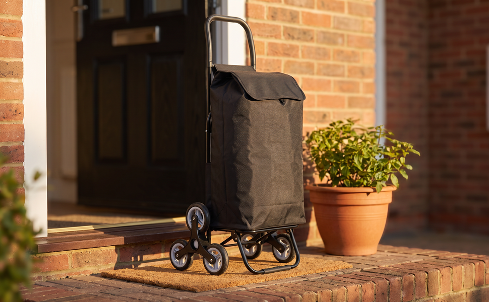Ezzyrol 74L 6-wheel stair climber shopping trolley in black standing at a front door beside a plant pot