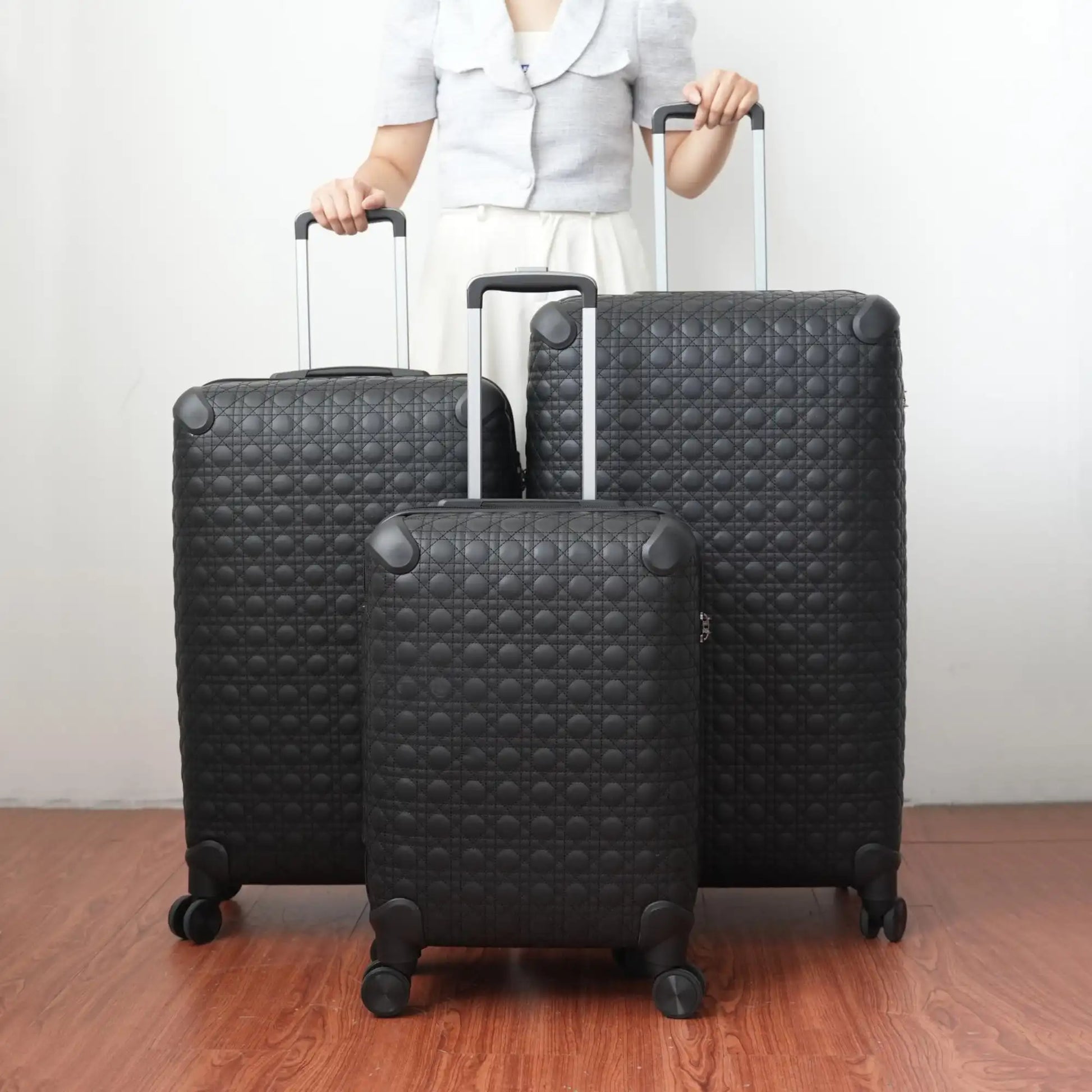 Person holding a set of black textured suitcases on a wooden floor.
