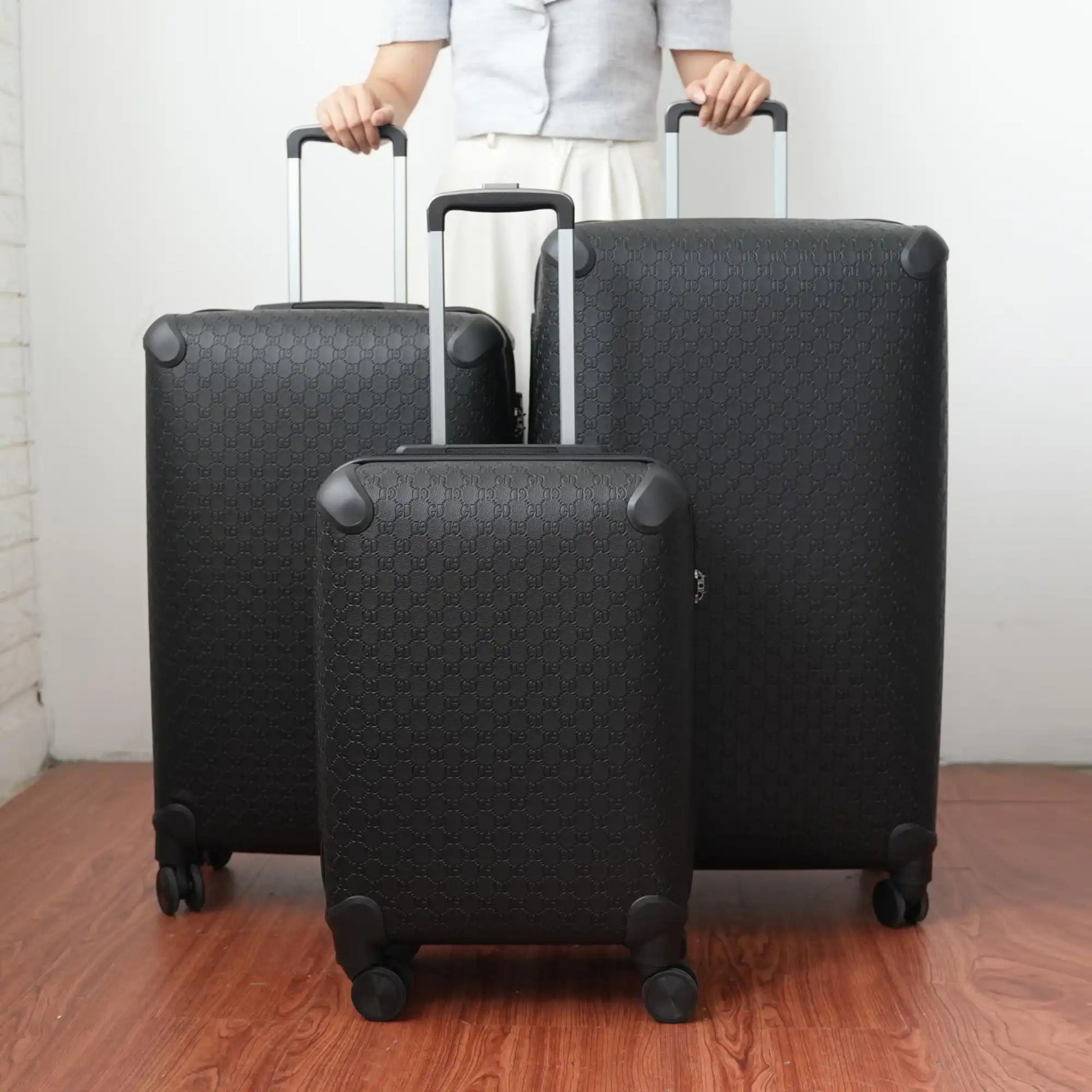 Three black suitcases of different sizes on a wooden floor with a neutral background