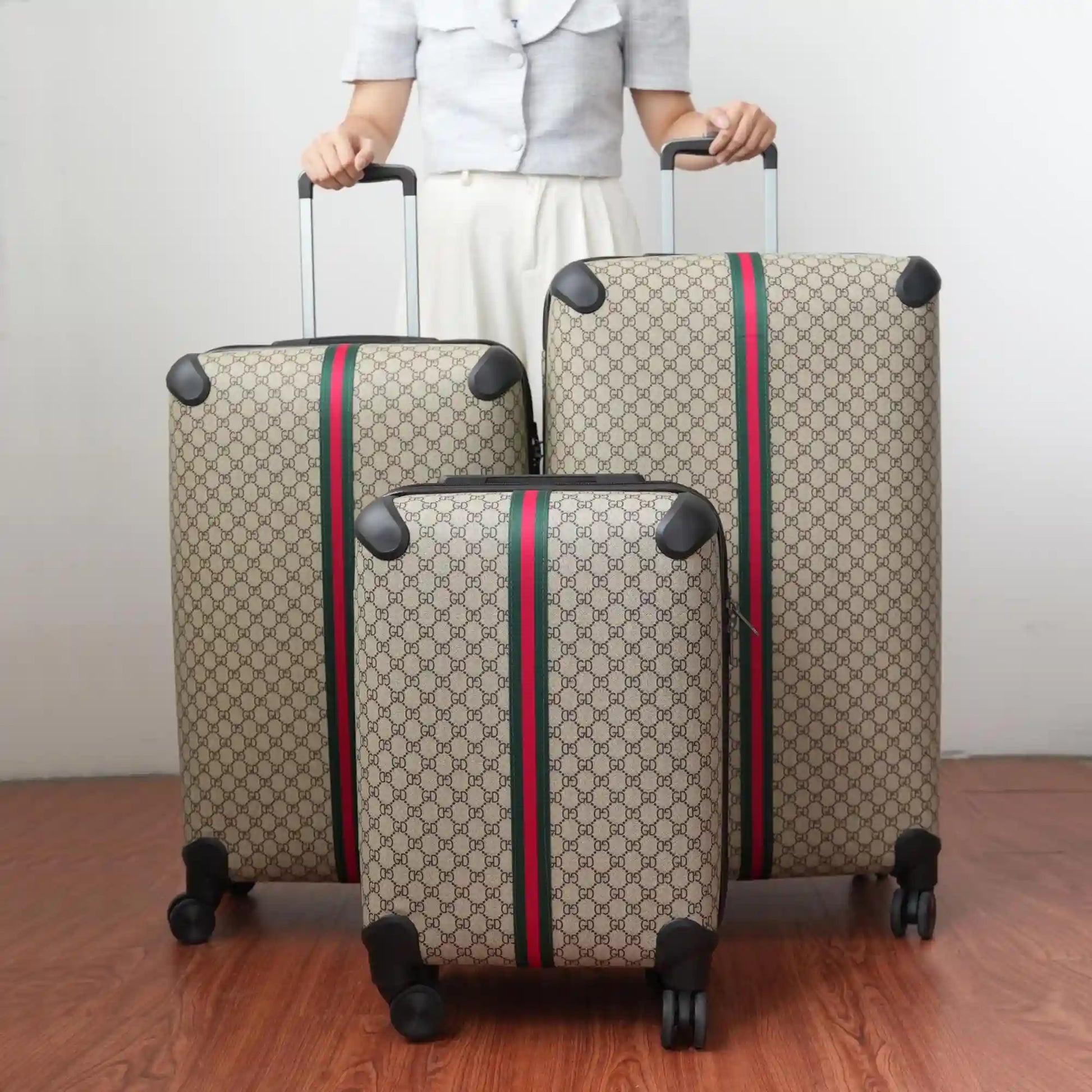 Three patterned suitcases with red and green stripes being held by a person on a wooden floor.