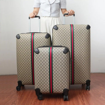 Three patterned suitcases with red and green stripes being held by a person on a wooden floor.