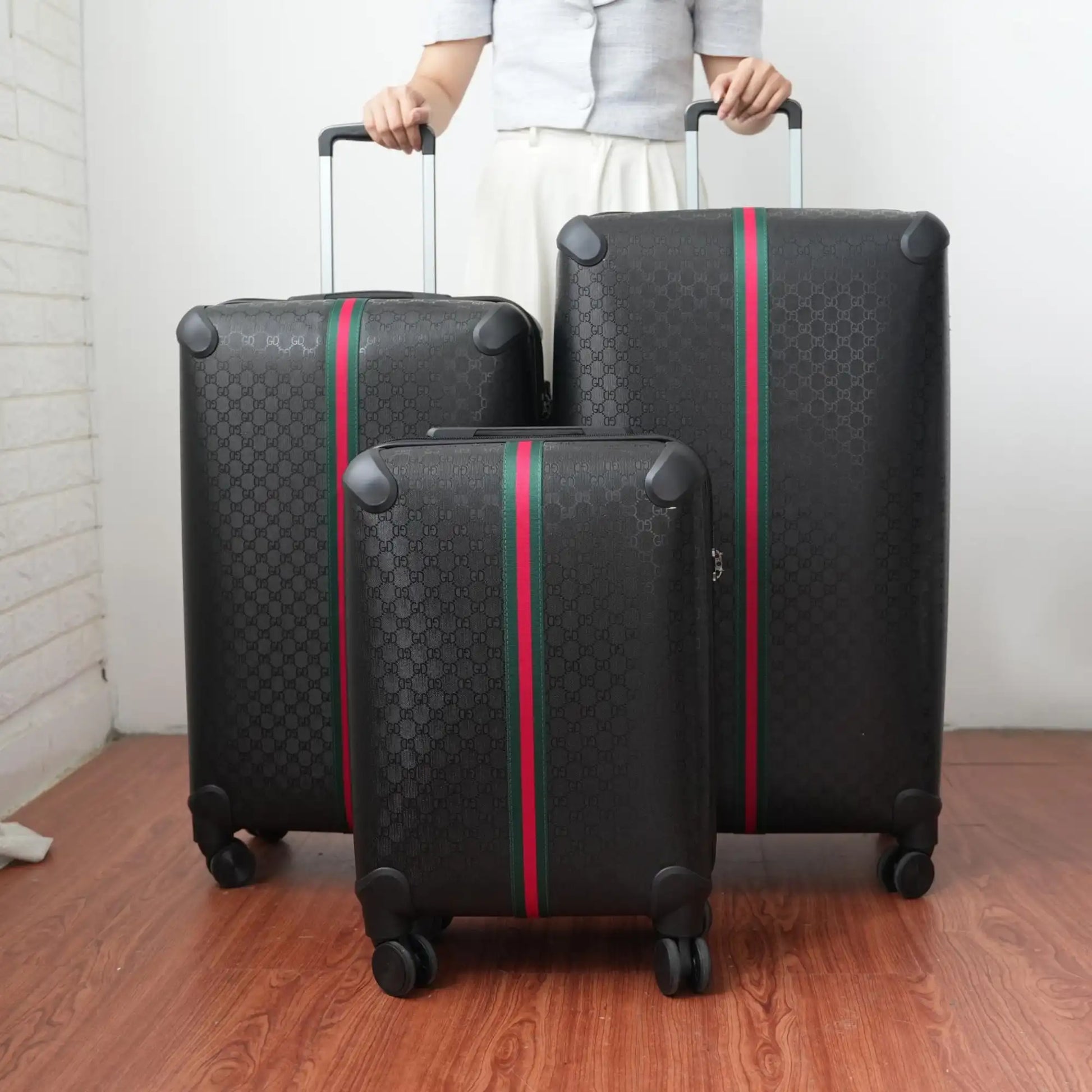 Three black suitcases with red and green stripes being held by a person on a wooden floor.