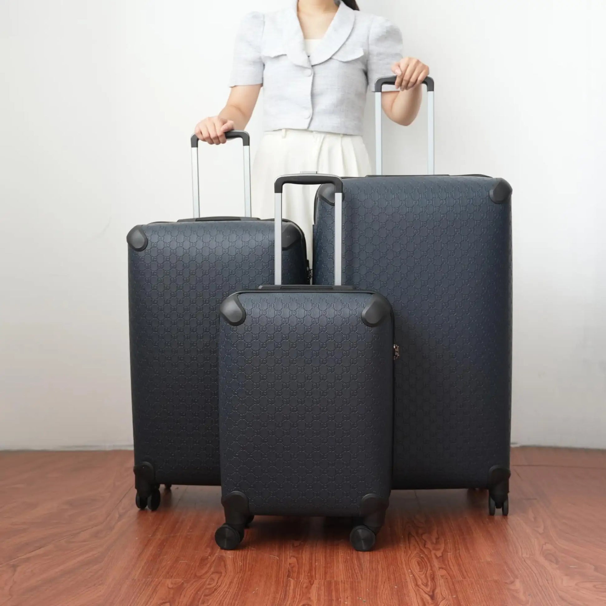 Person holding three dark gray suitcases on a wooden floor with a plain background