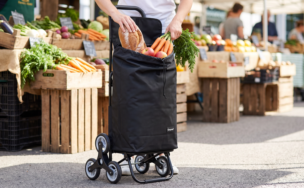 Ezzyrol 74L 6-wheel stair climber shopping trolley in black loaded with bread and carrots at a market stall