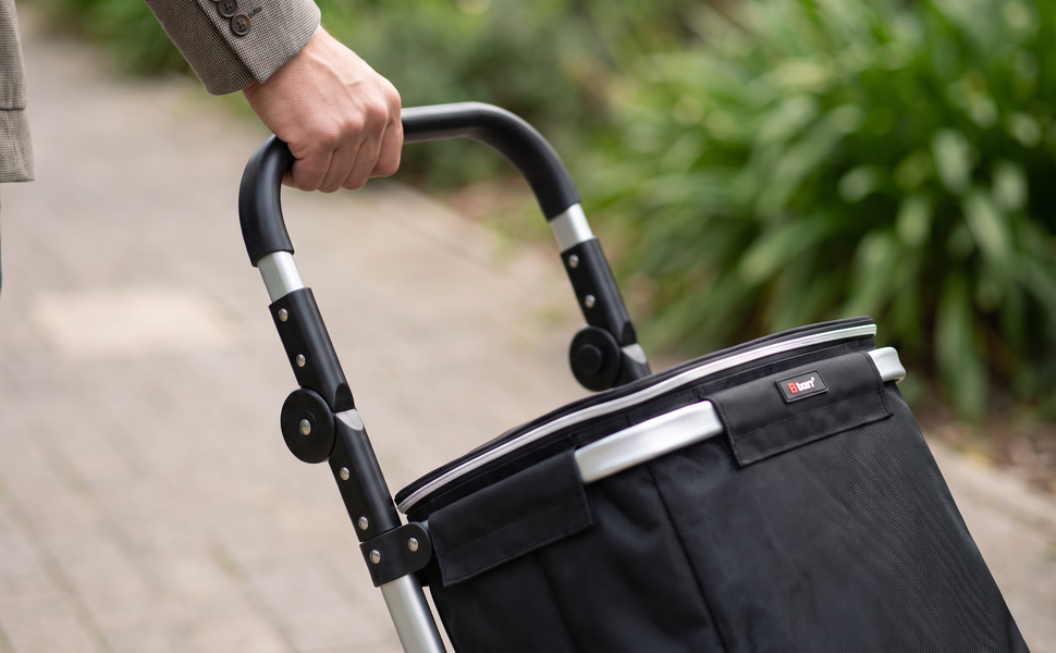 Hand resting on the padded handle of the black Ezzyrol 74L shopping trolley outdoors