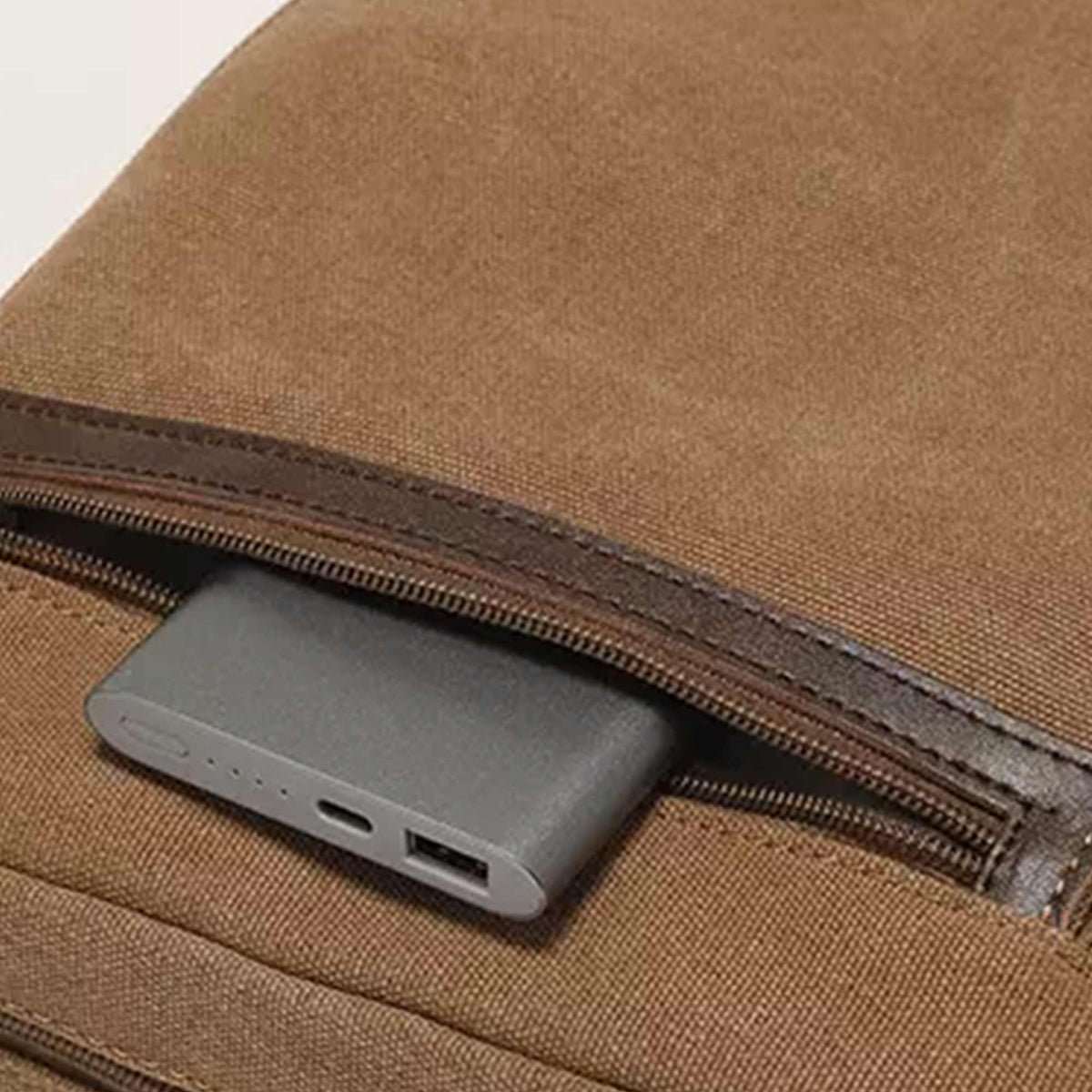 Close-up of the front zip pocket on the tan Grant crossbody bag, holding a power bank