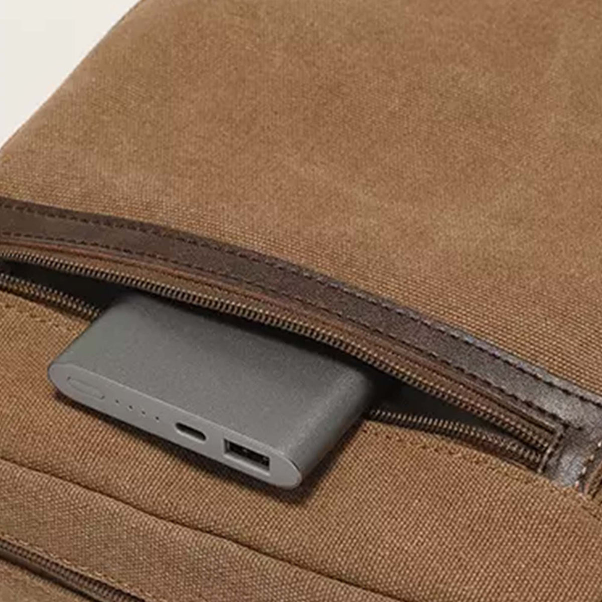 Close-up of the front pocket on the olive Grant crossbody bag with a power bank slipped in