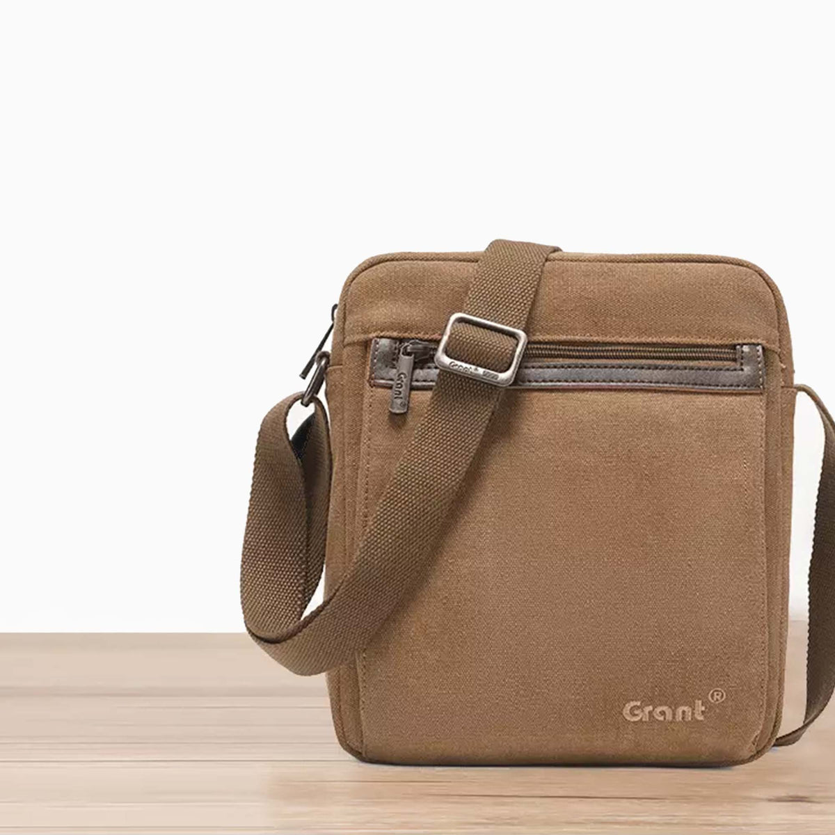 Grant compact canvas crossbody bag in tan canvas, front view on a wooden floor
