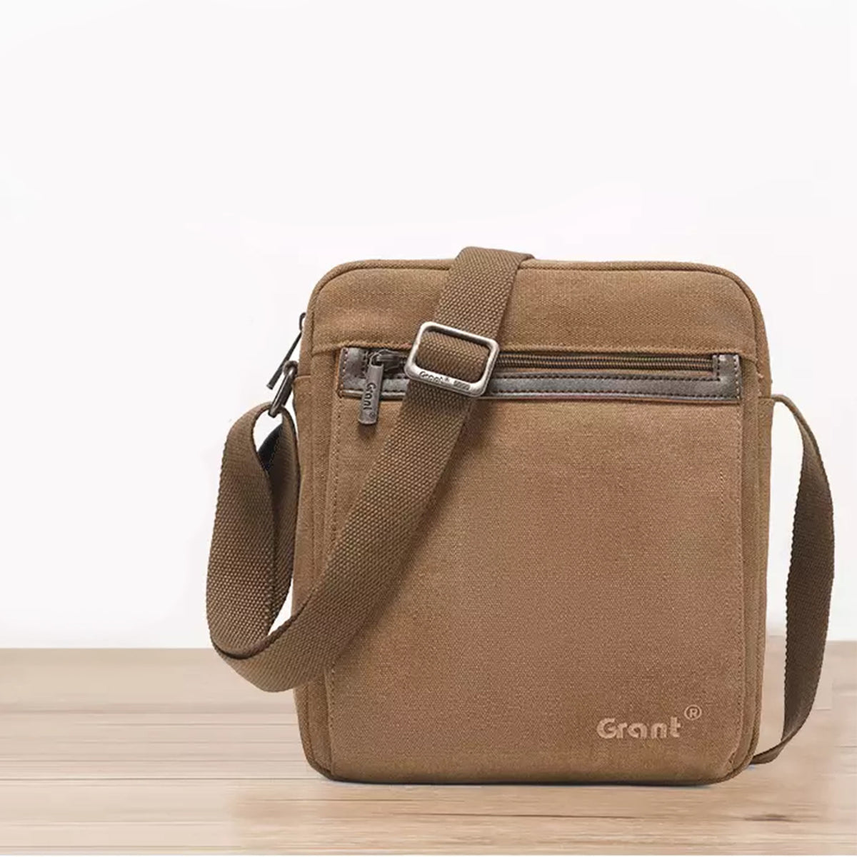 Grant compact canvas crossbody bag in tan canvas standing on a wooden surface