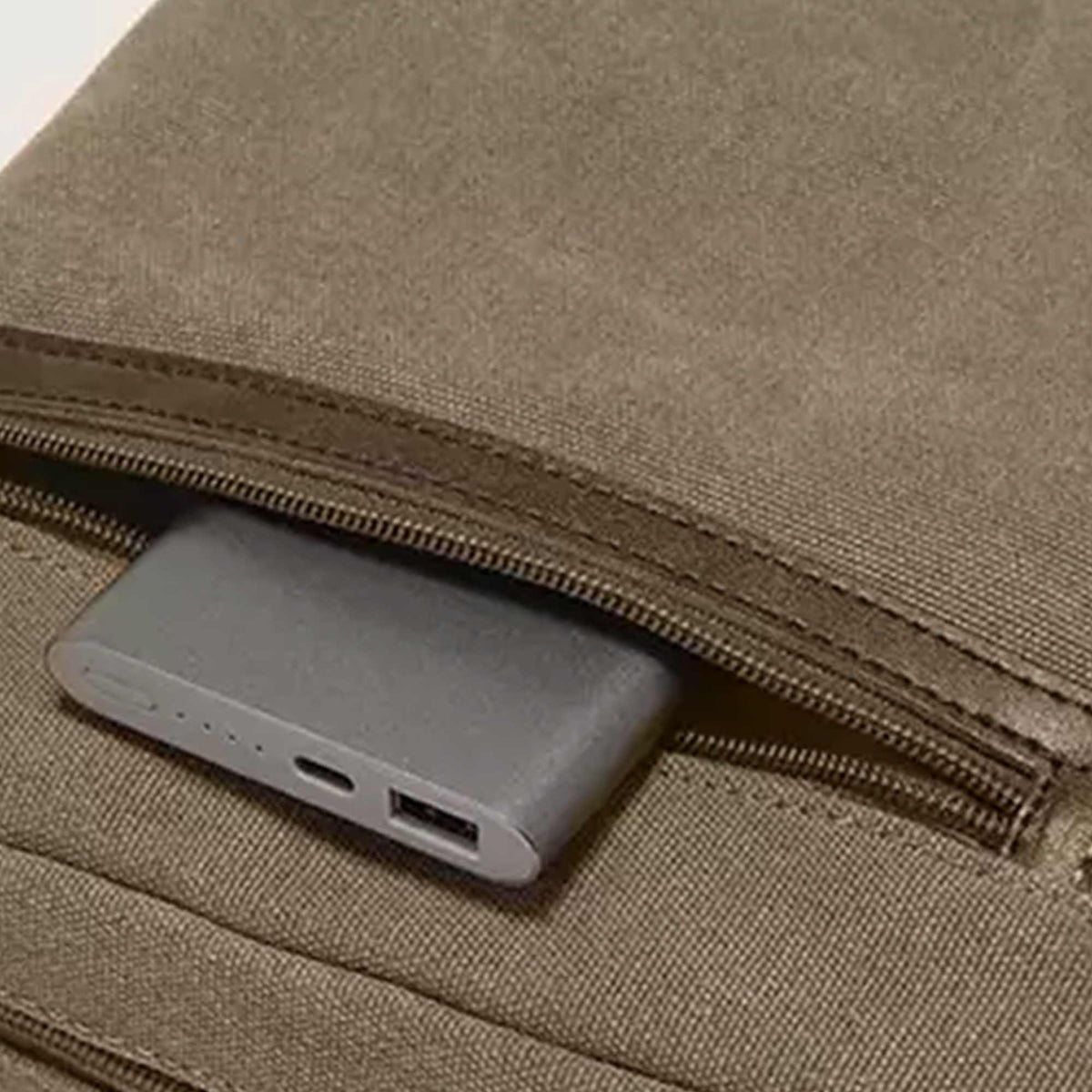 Front zip pocket of the olive Grant crossbody bag holding a power bank