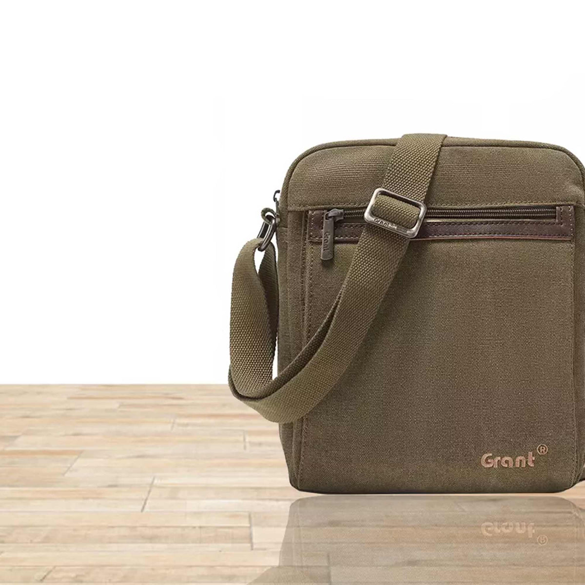 Grant compact canvas crossbody bag in olive canvas, front view on a wooden floor