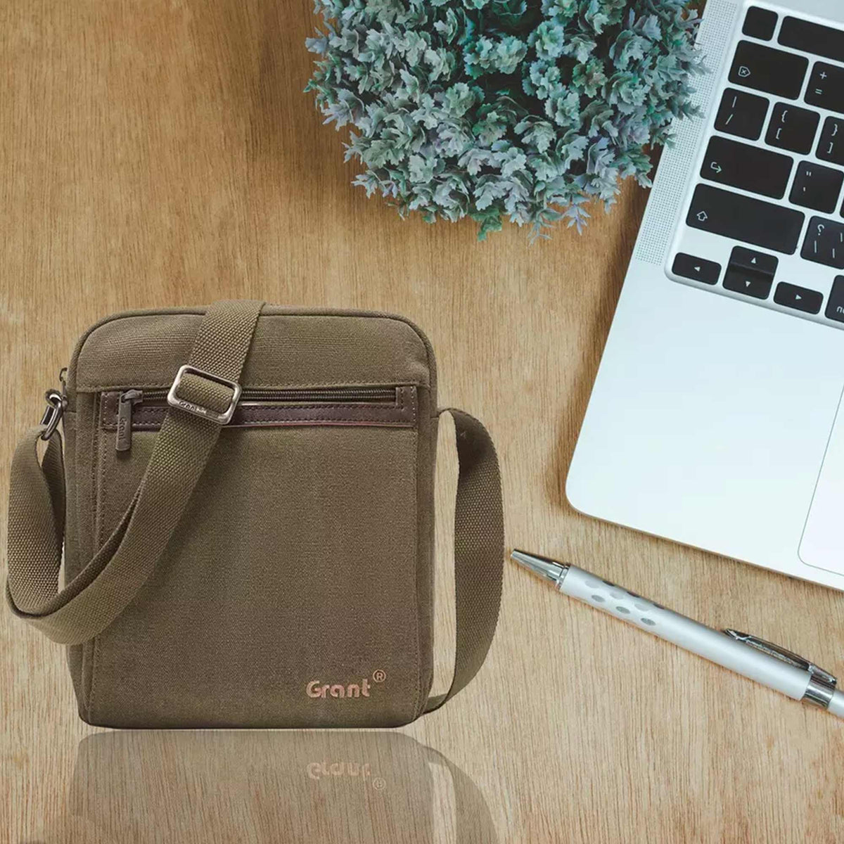 Grant compact canvas crossbody bag in olive canvas on a desk beside a laptop and a pen