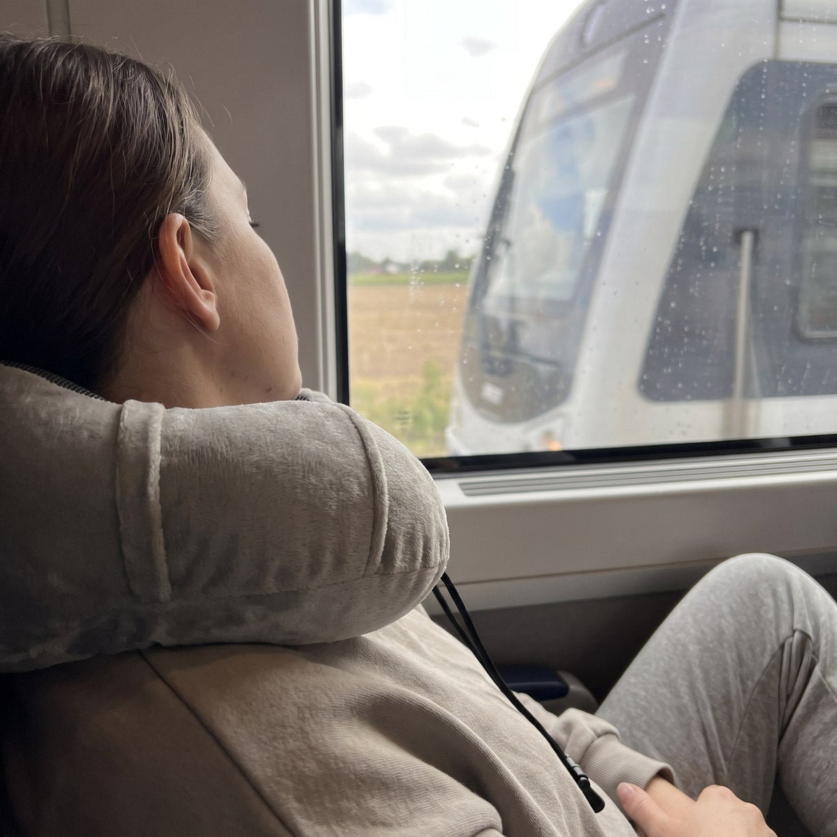 JUSTPACK Drift travel neck pillow in light grey, traveler resting by window