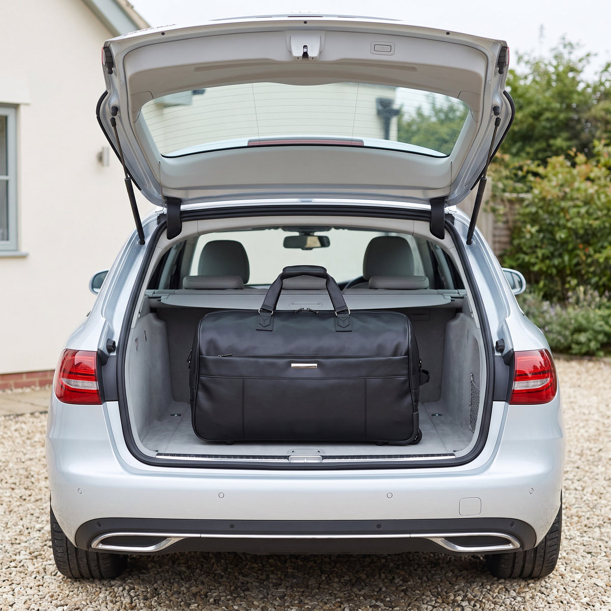 JUSTPACK Belgrave wheeled holdall in black faux leather loaded into the boot of an estate car on a driveway