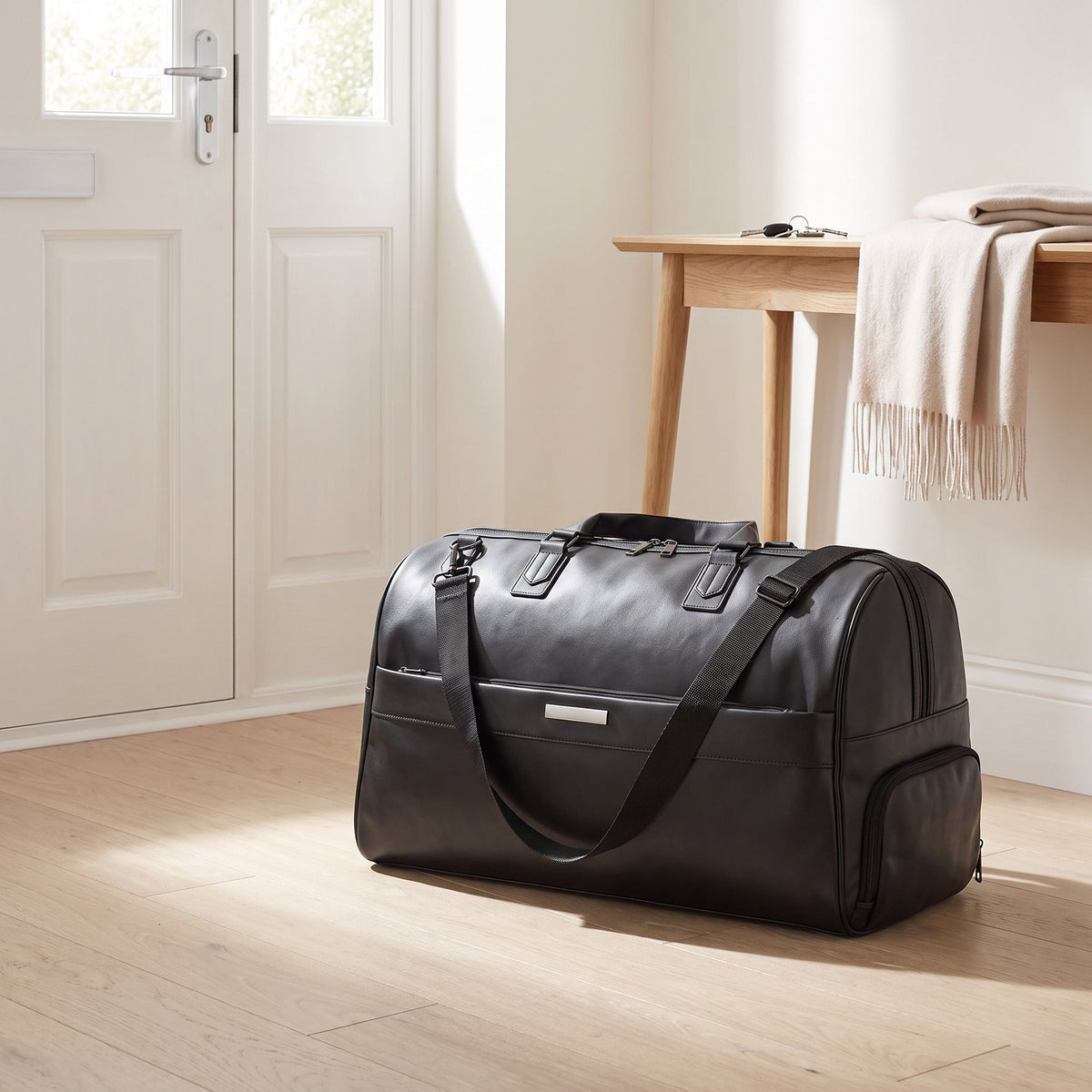 JUSTPACK Belgrave wheeled holdall in black faux leather packed and standing by the front door of a bright hallway