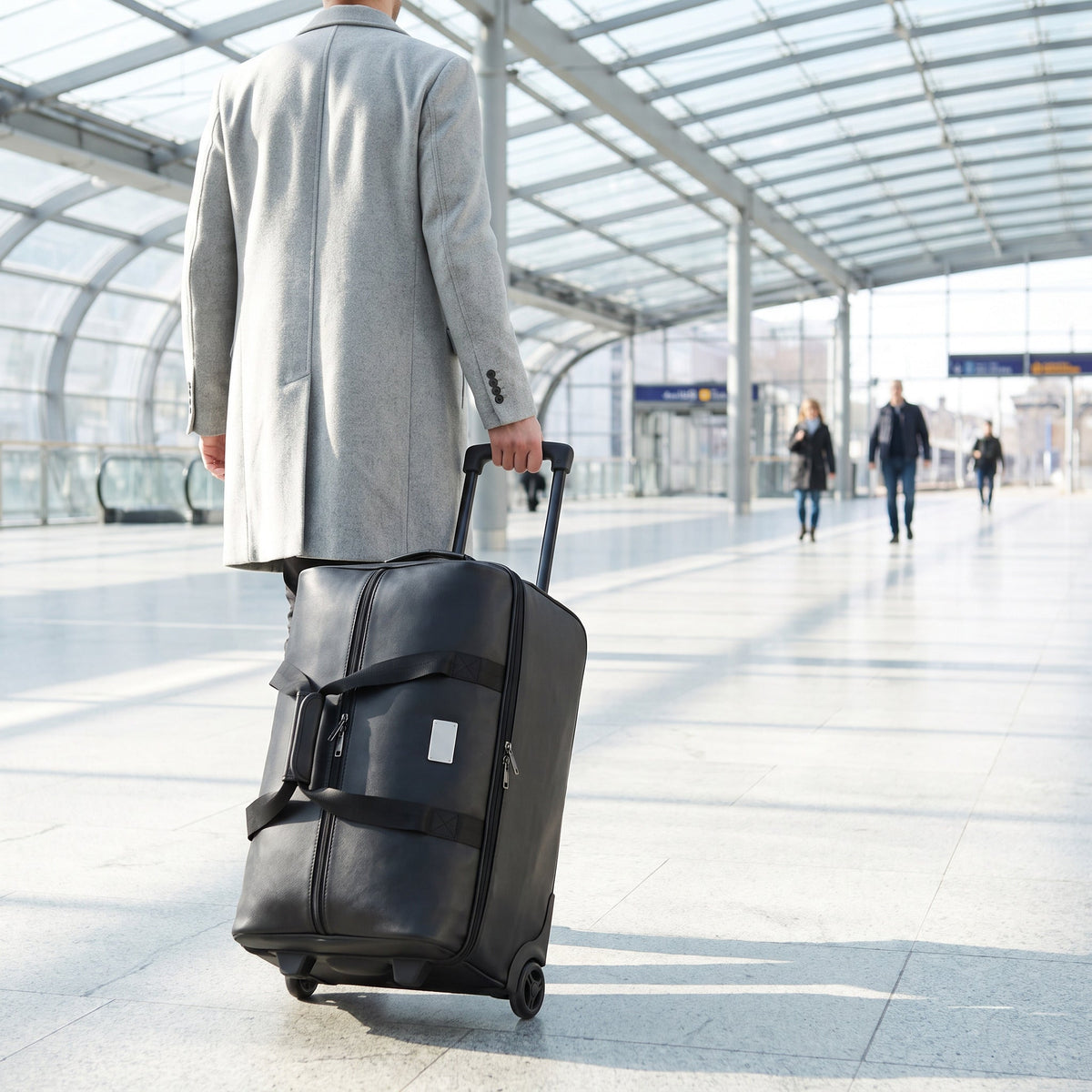 JUSTPACK Belgrave wheeled holdall in black faux leather wheeled along a daylit railway station concourse